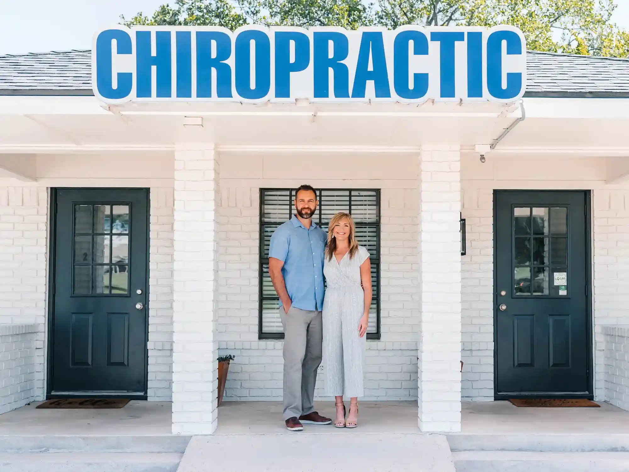 Two people standing outside a white brick chiropractic clinic